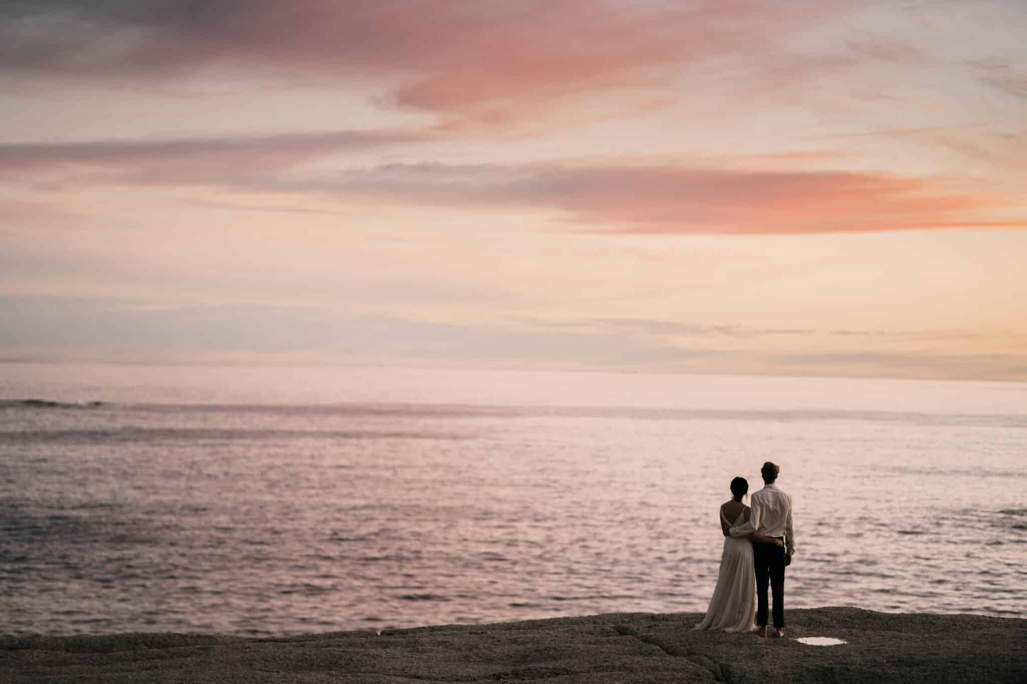 bride and groom looking over the water at sunset